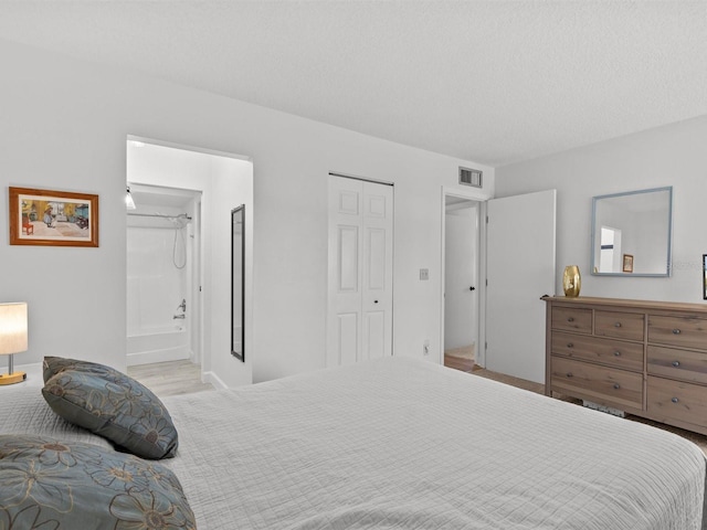 bedroom with ensuite bath, a closet, visible vents, and a textured ceiling