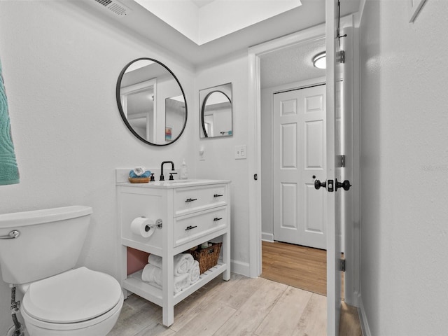 bathroom with baseboards, visible vents, toilet, wood finished floors, and vanity