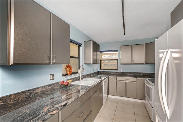 kitchen with white appliances, dark stone countertops, light tile patterned flooring, and sink