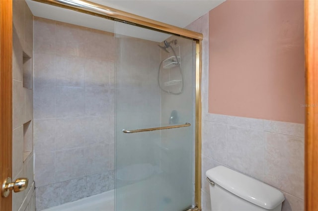 bathroom with tile walls, a shower with shower door, and toilet