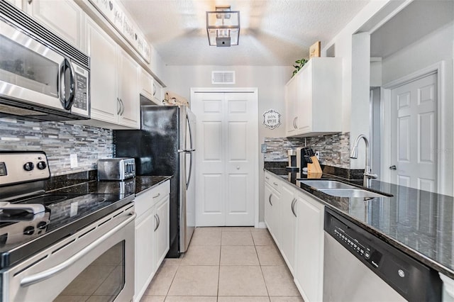 kitchen featuring white cabinets, appliances with stainless steel finishes, dark stone countertops, and sink