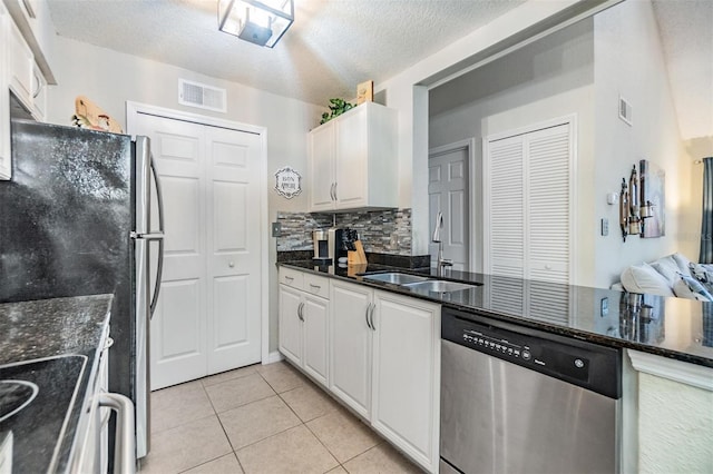 kitchen with sink, white cabinetry, light tile patterned flooring, dark stone countertops, and appliances with stainless steel finishes