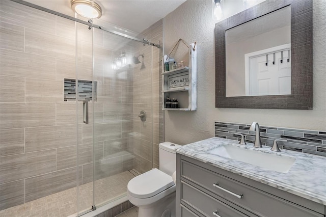 bathroom featuring toilet, a shower with door, vanity, and backsplash