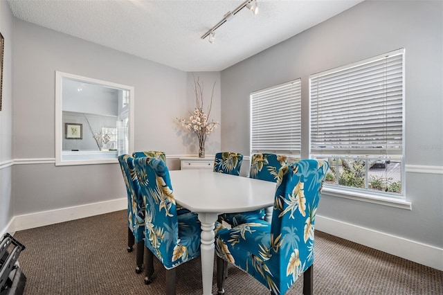 dining space featuring a textured ceiling, rail lighting, and dark colored carpet