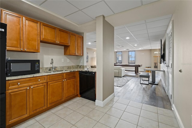 kitchen featuring black appliances, light tile patterned flooring, light stone counters, and sink