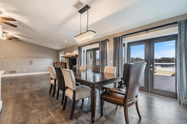 dining space featuring a water view, dark hardwood / wood-style flooring, french doors, lofted ceiling, and ceiling fan with notable chandelier