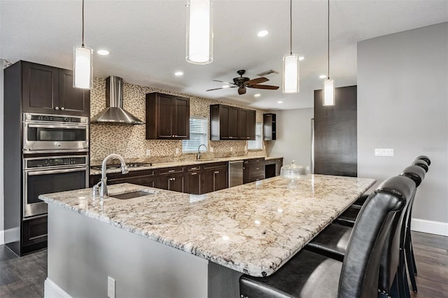 kitchen featuring ceiling fan, a spacious island, wall chimney exhaust hood, and sink