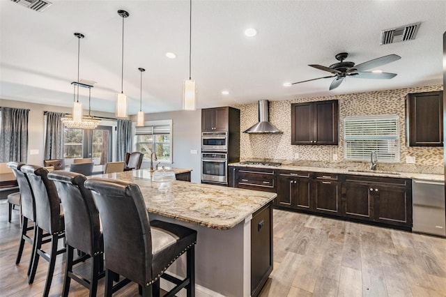 kitchen featuring a center island, a breakfast bar, sink, wall chimney range hood, and tasteful backsplash