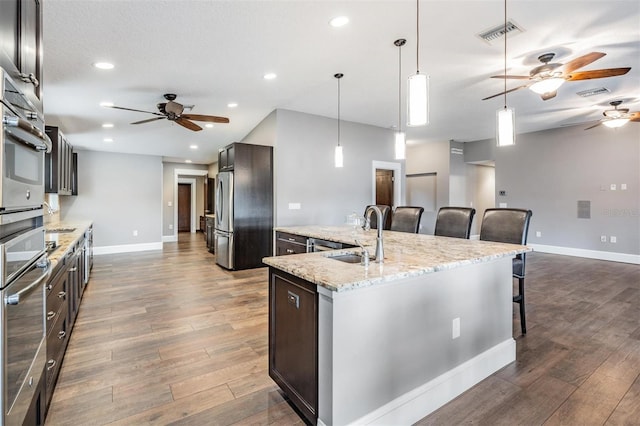 kitchen featuring a kitchen island with sink, a breakfast bar area, appliances with stainless steel finishes, sink, and decorative light fixtures