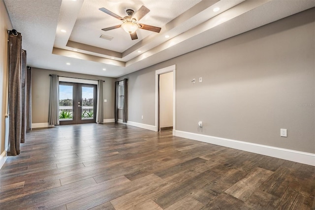 empty room featuring french doors, ceiling fan, a tray ceiling, and dark hardwood / wood-style flooring