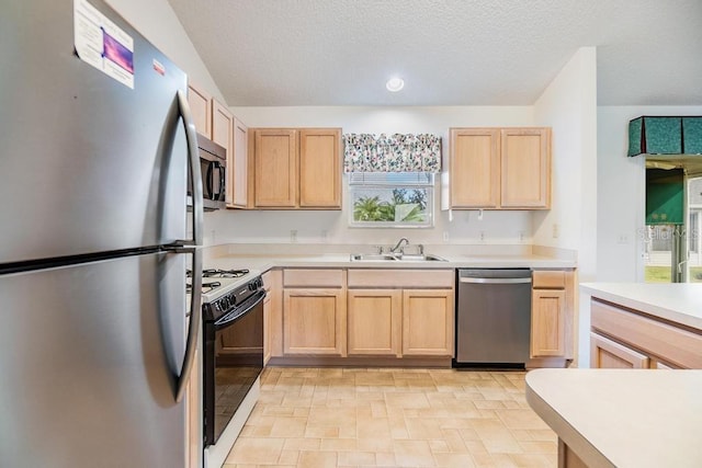 kitchen with a textured ceiling, stainless steel appliances, light brown cabinets, and sink