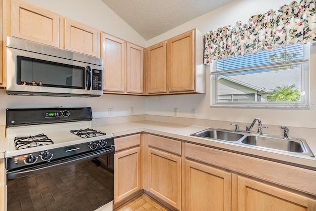 kitchen featuring gas stove, light brown cabinets, a textured ceiling, vaulted ceiling, and sink