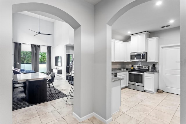 kitchen featuring appliances with stainless steel finishes, light stone countertops, ceiling fan, white cabinets, and light tile patterned flooring