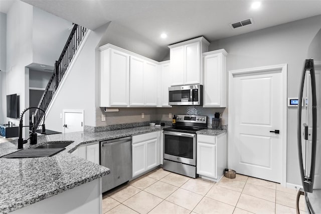 kitchen with appliances with stainless steel finishes, light tile patterned floors, light stone counters, sink, and white cabinetry