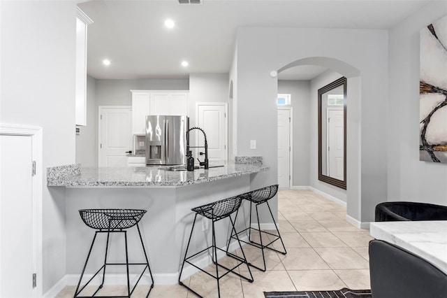 kitchen featuring light stone counters, white cabinetry, stainless steel refrigerator with ice dispenser, a breakfast bar area, and light tile patterned flooring