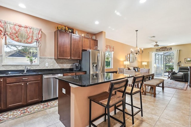 kitchen featuring a center island, light tile patterned flooring, sink, appliances with stainless steel finishes, and ceiling fan with notable chandelier