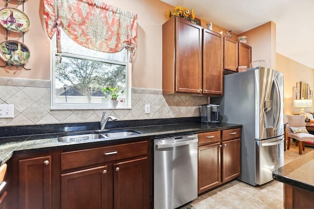 kitchen featuring stainless steel appliances, decorative backsplash, dark stone counters, and sink