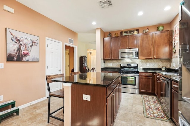 kitchen with light tile patterned floors, appliances with stainless steel finishes, backsplash, dark stone countertops, and a kitchen island