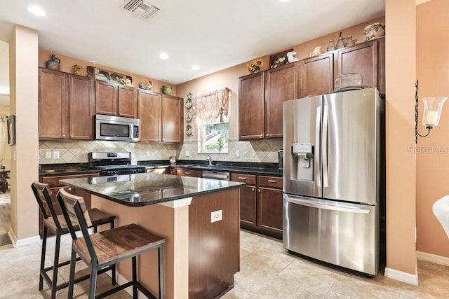 kitchen featuring a kitchen island, a kitchen bar, light tile patterned flooring, stainless steel appliances, and dark stone counters