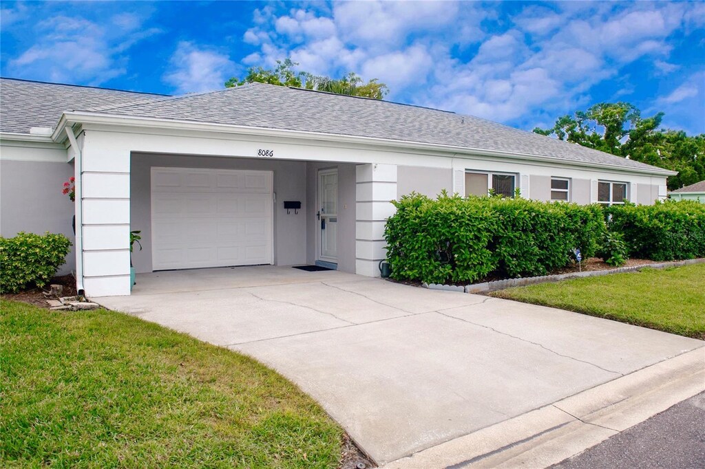 ranch-style home featuring stucco siding, driveway, a front yard, a garage, and a shingled roof
