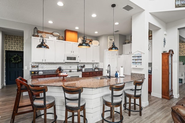 kitchen with sink, white cabinets, white appliances, hanging light fixtures, and a breakfast bar