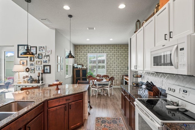 kitchen with decorative light fixtures, white cabinetry, white appliances, light hardwood / wood-style flooring, and dark stone counters