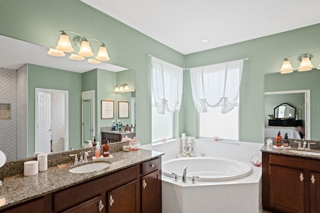 bathroom with tiled bath, an inviting chandelier, and vanity