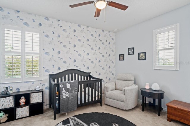 bedroom with ceiling fan, multiple windows, a crib, and light colored carpet