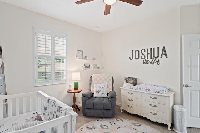 bedroom featuring ceiling fan, a crib, and light carpet