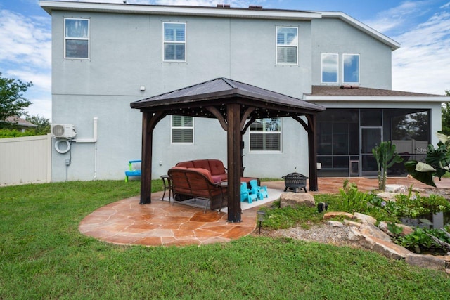 rear view of property with a lawn, a gazebo, a patio, an outdoor living space with a fire pit, and a sunroom