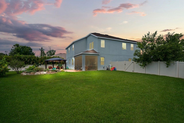 back house at dusk featuring a gazebo, a yard, and a sunroom