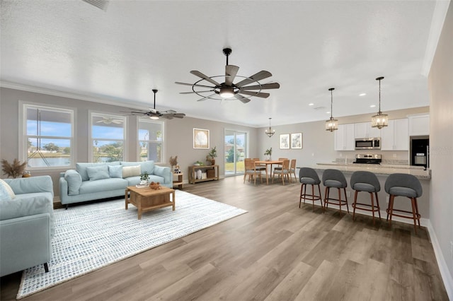 living room with ceiling fan, ornamental molding, light hardwood / wood-style floors, and a textured ceiling