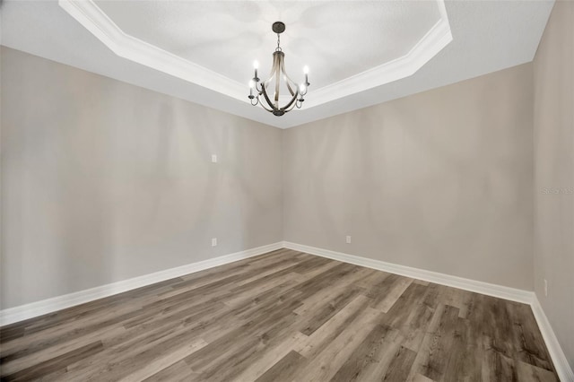 spare room featuring crown molding, a notable chandelier, a tray ceiling, and hardwood / wood-style flooring