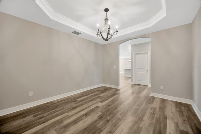 spare room featuring a chandelier, wood-type flooring, crown molding, and a raised ceiling