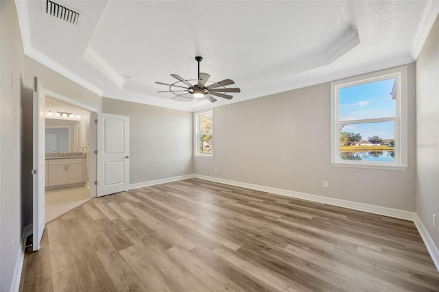 unfurnished bedroom featuring light hardwood / wood-style floors, crown molding, a raised ceiling, and ensuite bathroom