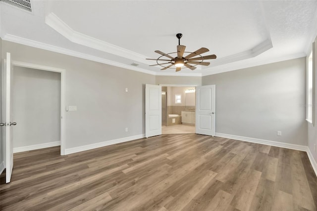 unfurnished bedroom with connected bathroom, hardwood / wood-style floors, ceiling fan, a tray ceiling, and crown molding