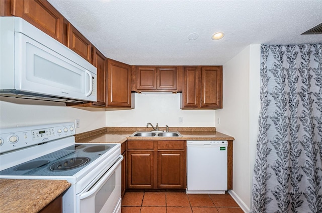 kitchen featuring sink, white appliances, light tile patterned floors, and a textured ceiling