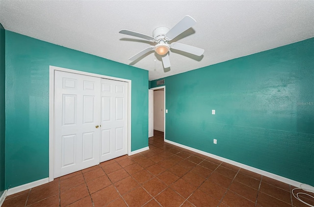 unfurnished bedroom with dark tile patterned floors, ceiling fan, and a closet