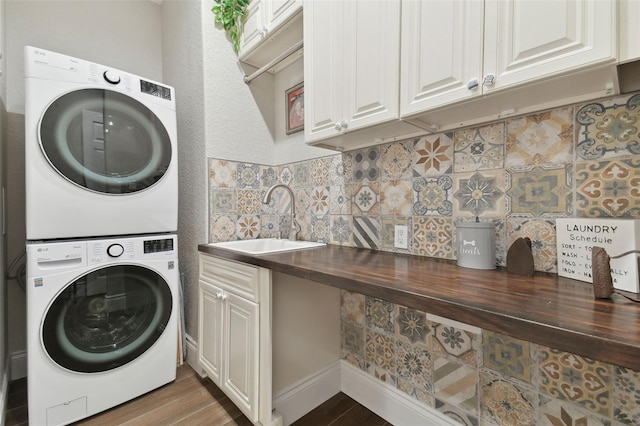 laundry room featuring a sink, cabinet space, wood finished floors, and stacked washing maching and dryer