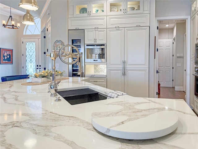 kitchen with oven, light stone counters, decorative light fixtures, white cabinetry, and glass insert cabinets