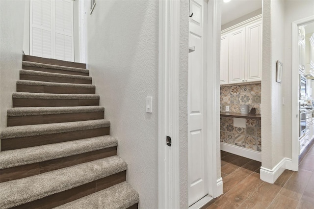 stairs with wood finish floors, baseboards, and a textured wall