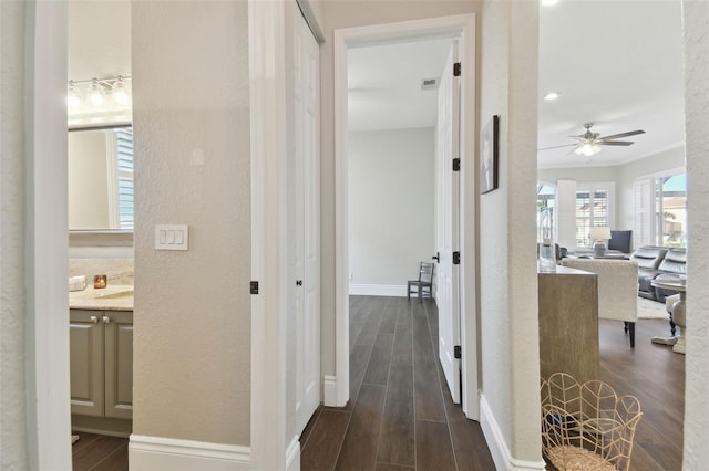 hall with wood finish floors, baseboards, ornamental molding, and a textured wall