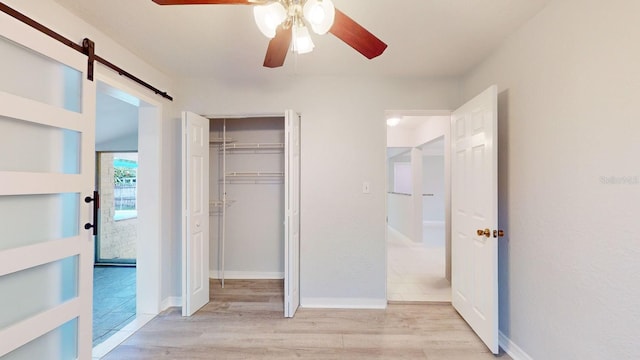 interior space with ceiling fan, light hardwood / wood-style floors, a closet, and a barn door