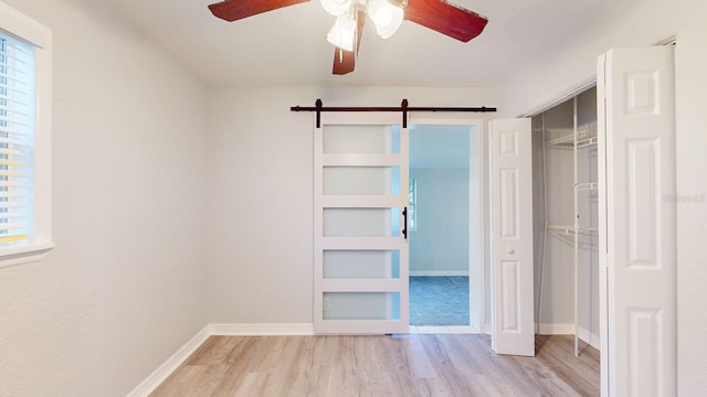 unfurnished bedroom with ceiling fan, light hardwood / wood-style floors, a closet, and a barn door