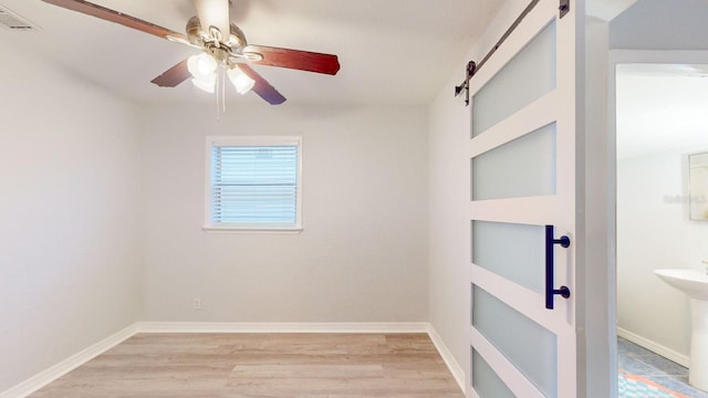 empty room with sink, light wood-type flooring, ceiling fan, and a barn door