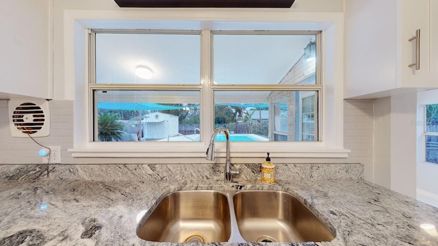 room details featuring sink, decorative backsplash, white cabinetry, and light stone countertops