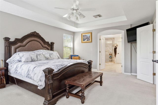 bedroom with ceiling fan, ensuite bathroom, a raised ceiling, and light carpet