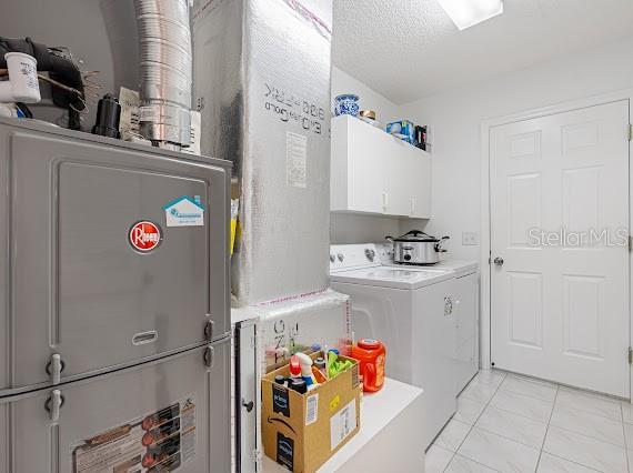 laundry area with washer and clothes dryer, light tile patterned floors, and cabinets