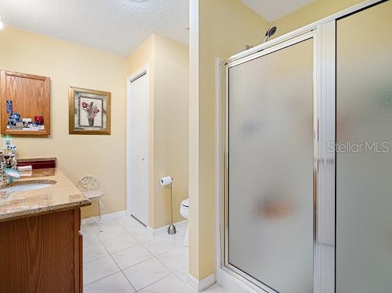 bathroom with tile patterned flooring, an enclosed shower, toilet, a textured ceiling, and vanity