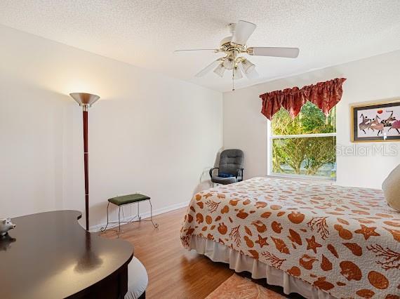 bedroom with hardwood / wood-style flooring, a textured ceiling, and ceiling fan